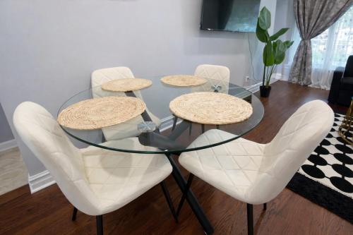 a glass table with four white chairs around it at Newly Renovated 3BR North York Bungalow with Backyard Patio & Volleyball Set! Close to Rogers Stadium, TTC Subway Access, Perfect for Family Travel, Group Trips & Work Stays! in Toronto