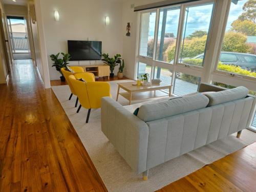 a living room with a white couch and yellow chairs at Sitara Cottage in Yanakie
