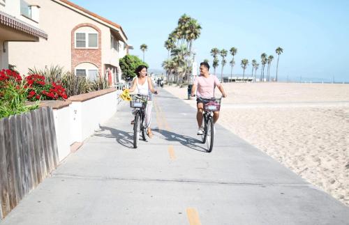 two people riding bikes down a sidewalk on the beach at Charming 2Br Condo W Ac, Steps To Beach And Balboa Pier By Beachview Rentals in Newport Beach