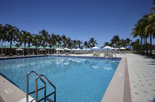 a large swimming pool with palm trees and umbrellas at Sea View Hotel in Miami Beach