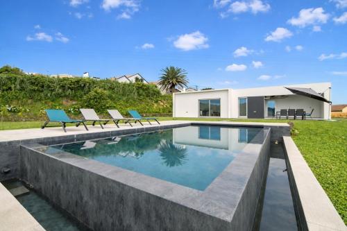 a swimming pool with two blue chairs next to a house at Seaview Villa with Heated Private Pool in Bretanha