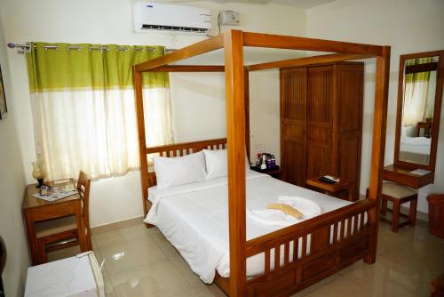 a bedroom with a wooden canopy bed with white sheets at BigStay Apart Hotel in Tada