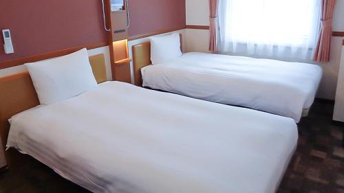 two beds in a hotel room with white sheets at Toyoko Inn Fujisan Numazu eki Kita guchi No 2 in Numazu