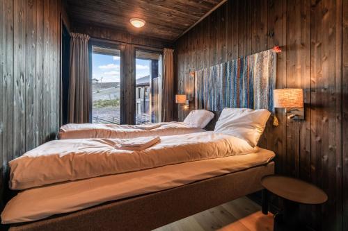 two beds in a room with wooden walls and a window at Kikut Alpin Lodge 2102 in Hol