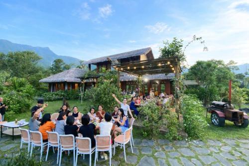 a group of people sitting at a table in front of a house at Orchid Villa & Homestay Farm Lăng Cô in Thôn An Cư Ðông