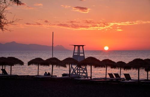 a beach with chairs and a lifeguard tower at sunset at Aqua Blue Beach Hotel in Perissa
