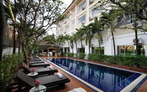 a hotel swimming pool with lounge chairs and trees at Harmony Indochine d'Angkor in Siem Reap