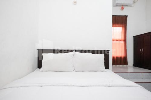 a bed with white sheets and pillows in a bedroom at Katup Guest House Syariah Mitra RedDoorz in Yogyakarta