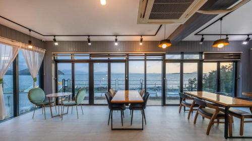 a dining room with tables and chairs and large windows at Yeosu Eoneumeosjinnal Pension in Yeosu