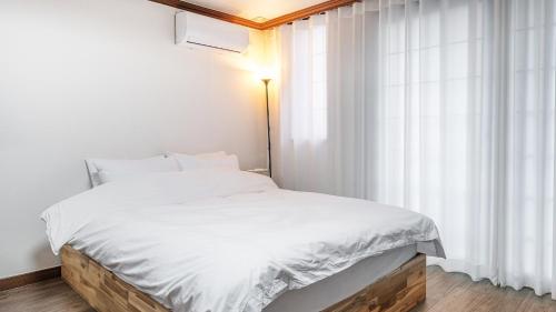 a bedroom with a bed with white sheets and a window at Geoje Blueberry Pet Pension in Geoje