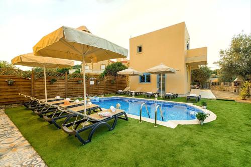 a pool with chairs and umbrellas next to a house at Lindos Luxury Retro Villas in Lindos