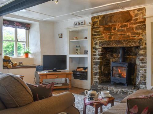 a living room with a stone fireplace and a television at Horseshoe Cottage in Starbotton