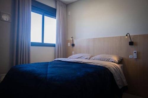 a bedroom with a bed with a blue blanket and a window at Studio Completo Perto Hospital e Shopping in Tubarão