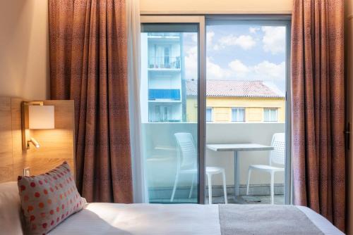 a bedroom with a bed and a balcony with a table at Hôtel L'Empreinte in Cagnes-sur-Mer