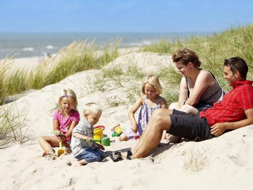 a family sitting in the sand at the beach at 4 star holiday home in Ringkøbing in Ringkøbing