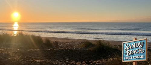 a sign on a sandy beach with the ocean at Hooper's Sandy Beach Guest Rooms in Swansea