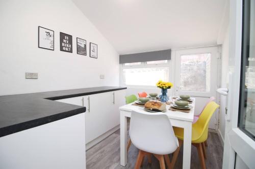a white kitchen with a white table and yellow chairs at Afan House by STAE-Homes in Glyncorrwg