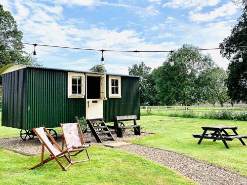 a green shed with a picnic table and benches at The Shepherds Huts in Ormesby Saint Michael