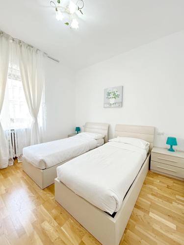 two beds in a bedroom with white walls and wood floors at Affittacamere Seveso in Milan