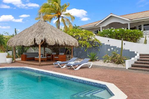 a villa with a swimming pool and a straw umbrella at Villa Strelitzia in Dorp Soto