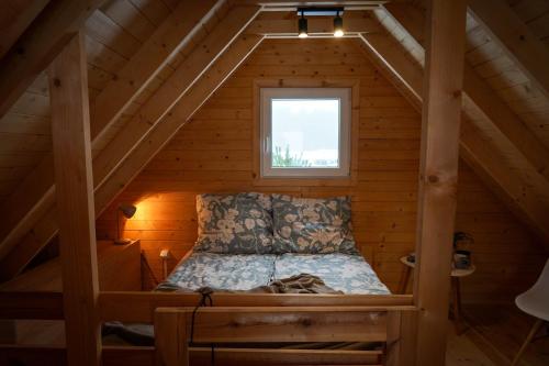 a bed in a wooden cabin with a window at Domek Pod Sosnami in Bronków
