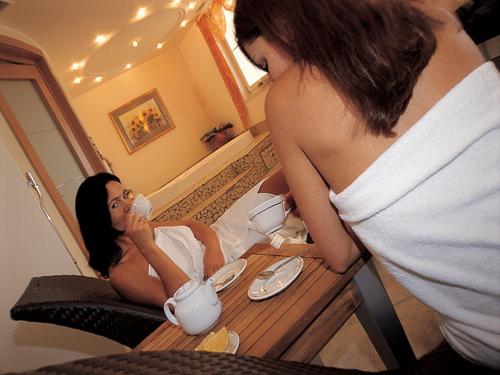 a woman sitting at a table drinking from a tea kettle at Hotel Comfort Erica Dolomiti Val d'Adige in Salorno sulla Strada del Vino