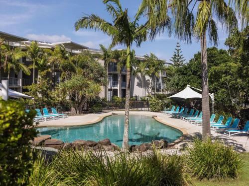 a swimming pool with blue chairs and palm trees at Peppers Salt Resort & Spa in Kingscliff