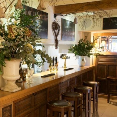 a bar with stools and a counter with flowers at The Bell at Hampton Poyle in Kidlington
