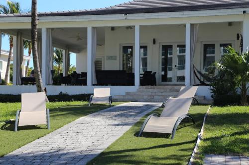 a group of white chairs in front of a house at Amamare Waterfront Villa | Pool + Private Dock in Bailey Town
