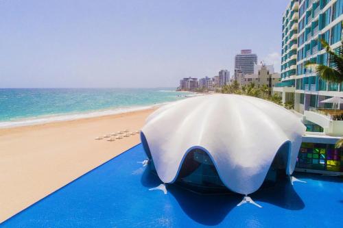 a large white umbrella on the beach next to a building at La Concha Resort, Puerto Rico, Autograph Collection in San Juan