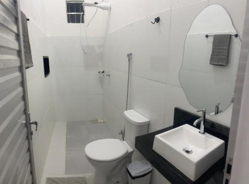 a white bathroom with a toilet and a sink at Suítes JK in Paragominas