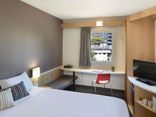 a hotel room with a bed and a desk and a window at ibis Newcastle in Newcastle