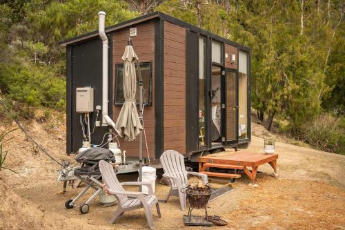 a black tiny house with chairs and an umbrella at Wattle Grove Hideaway by Tiny Away in Wattle Grove