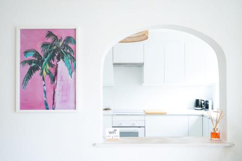 a white kitchen with a palm tree painting on the wall at The Chelsea Beachside Apartment in The Entrance