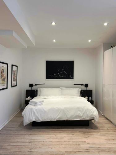 a white bedroom with a large bed with a tv on the wall at Luxury Executive Studio in Oakville