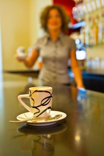 a coffee cup on a counter with a woman in the background at Hotel Goldener Stern in Caldaro