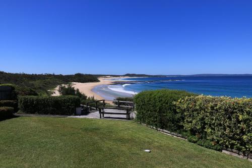 a bench sitting on the grass near a beach at Bunkys By The Sea Holiday House in Berrara