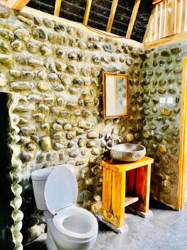 a bathroom with a toilet and a stone wall at Triple J Villa in Sekongkang Bawa