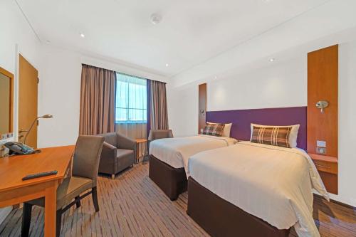 a hotel room with two beds and a desk at Premier Inn Abu Dhabi Airport Business Park in Abu Dhabi
