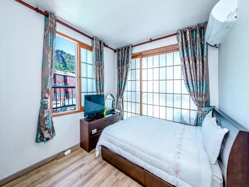 a bedroom with a bed and a tv and windows at Sea Dragon Pension in Seogwipo