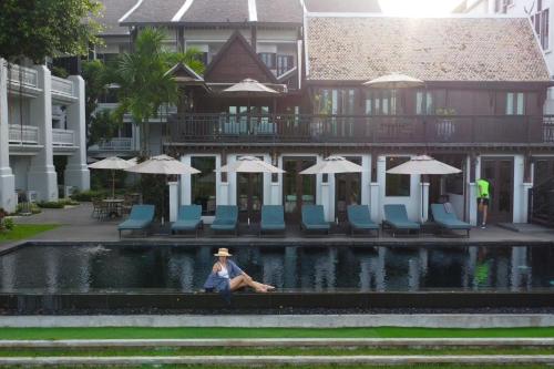 a person sitting next to a fountain with chairs and umbrellas at Buri Sriping Riverside Resort & Spa in Chiang Mai