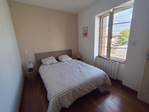 a bedroom with a bed with a striped comforter and a window at La petite Amandaise in Saint-Amand-sur-Sèvre
