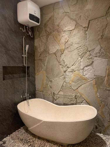 a bath tub in a bathroom with a stone wall at Kamaya Villa Jogja in Ngaglik