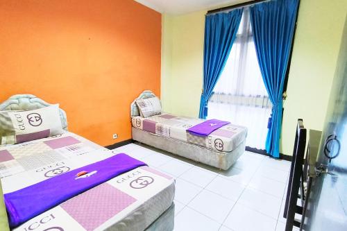 two beds in a room with blue curtains at Hotel Pattimura powered by Cocotel in Stasiun Tawang