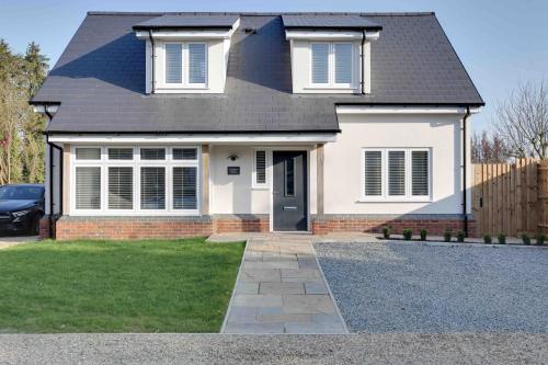 a white house with a black roof and a driveway at Foxglove House & Hot Tub Stansted Airport in London Stansted Airport