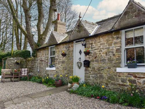 an old stone house with flowers in front of it at Fern Cottage in Bardon Mill