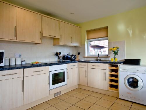 a kitchen with white cabinets and a washer and dryer at Beech Lodge - Retallack Resort in Saint Columb Major