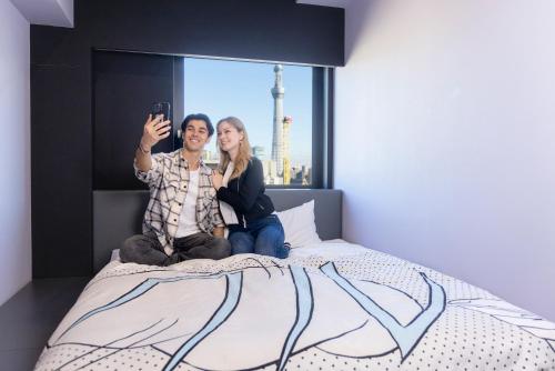two women sitting on a bed taking a picture at HOTEL TAVINOS Asakusa in Tokyo