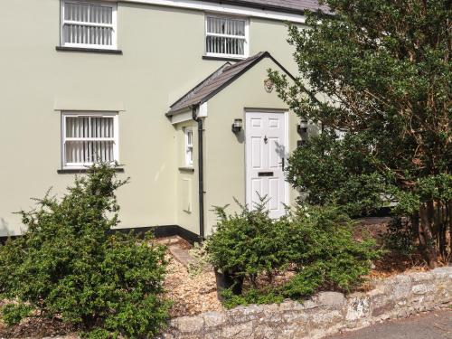 a white house with a white door and some bushes at Holly Cottage in Angle