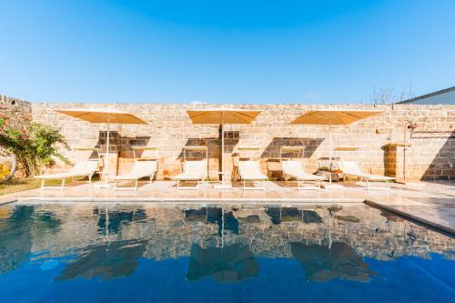 a pool with chairs and umbrellas next to a brick wall at Masseria Lovetere Rooms - Salento Selection in Copertino